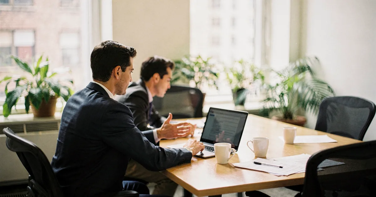 Two advisers review figures on a laptop at a conference table in a bright Hackensack office